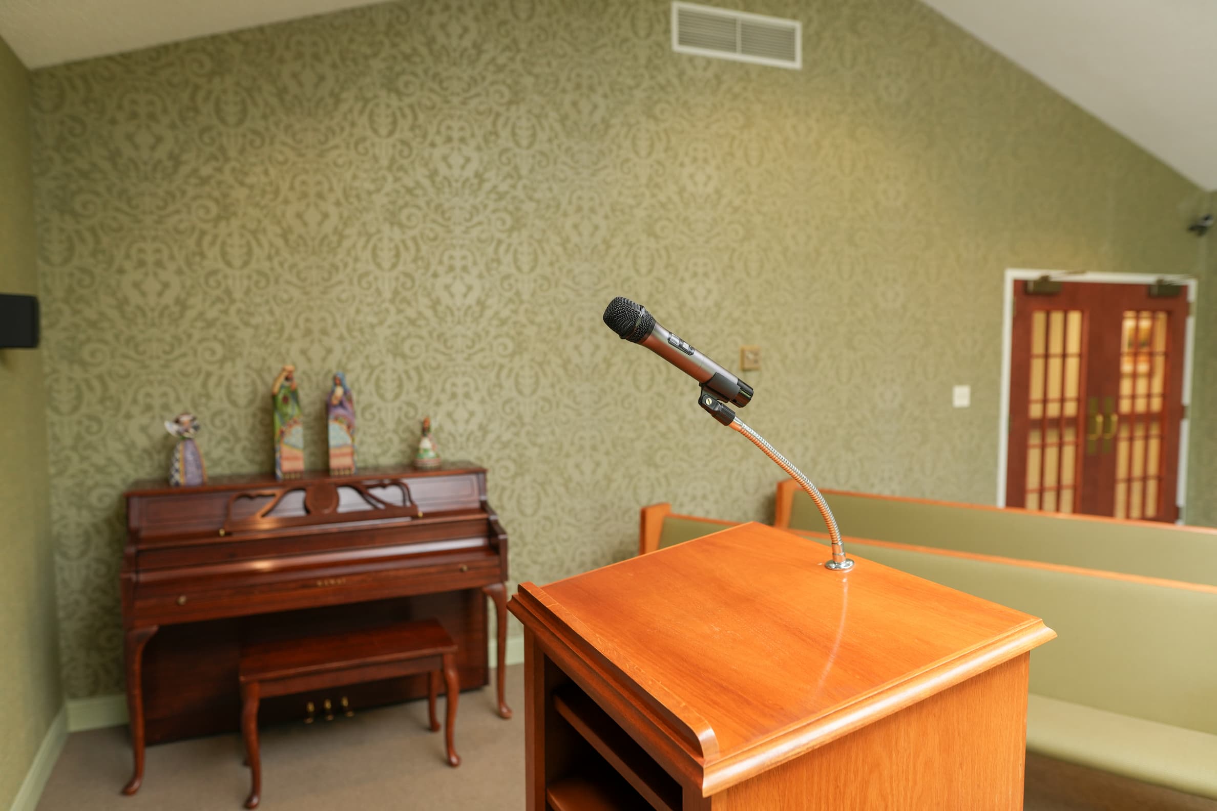 Community gathering area with lectern, microphone, and piano near upholstered benches.