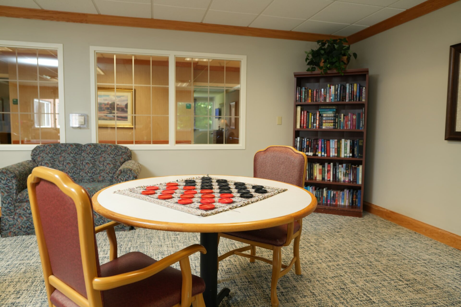 Community room with checkers table, bookcase, and seating in a residential building.