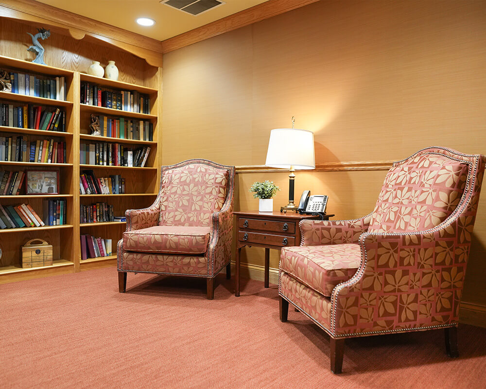 Cozy library corner with armchairs and bookshelves in a senior living community unit.