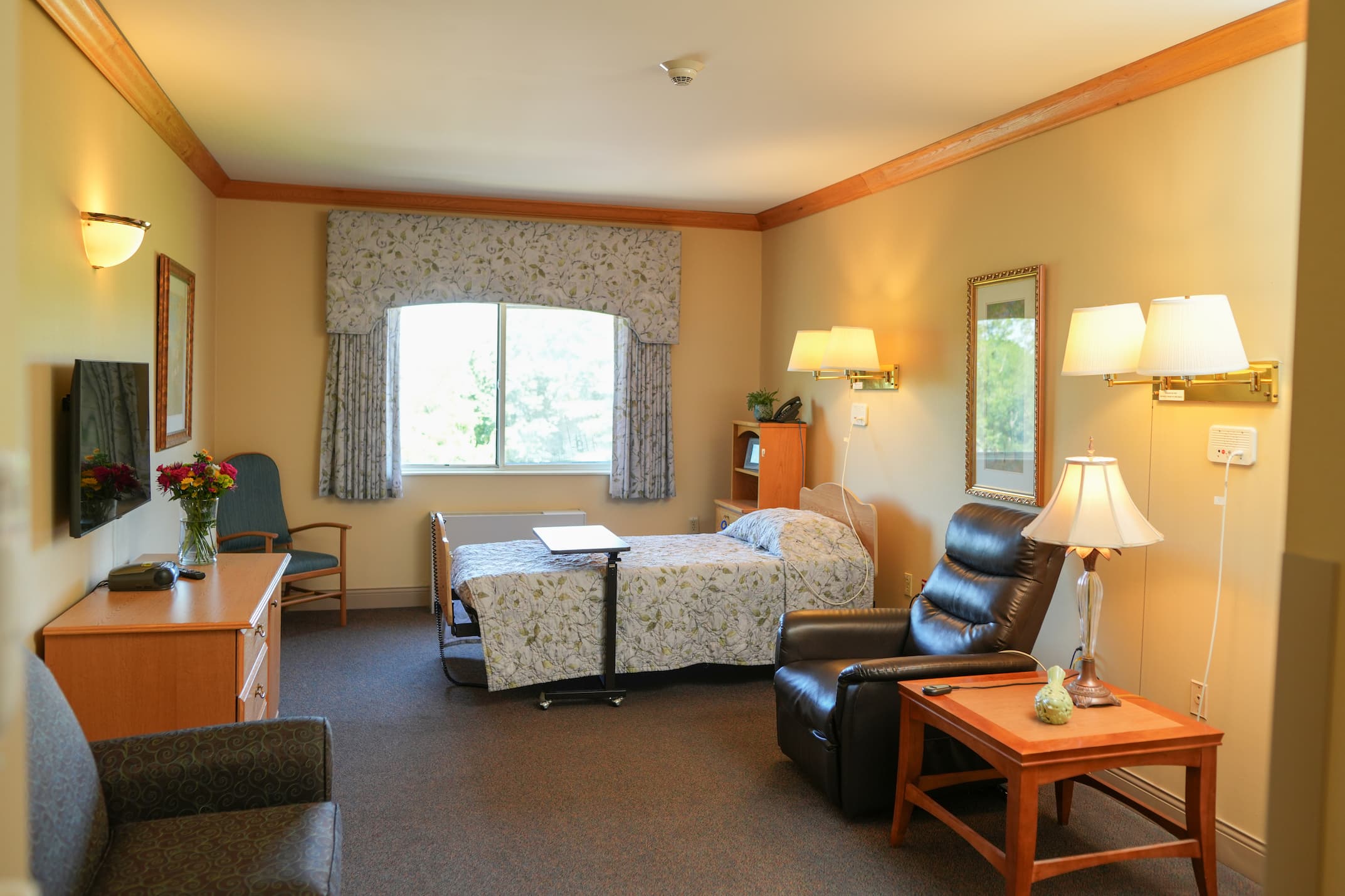 Comfortable living unit with bed, recliner, and window view in a senior community.