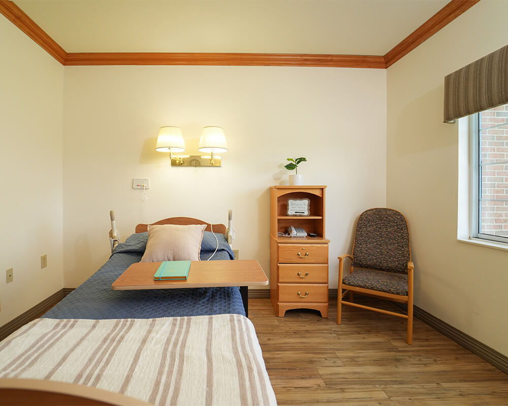 Comfortable unit in senior community with a bed, table, chair, and window.