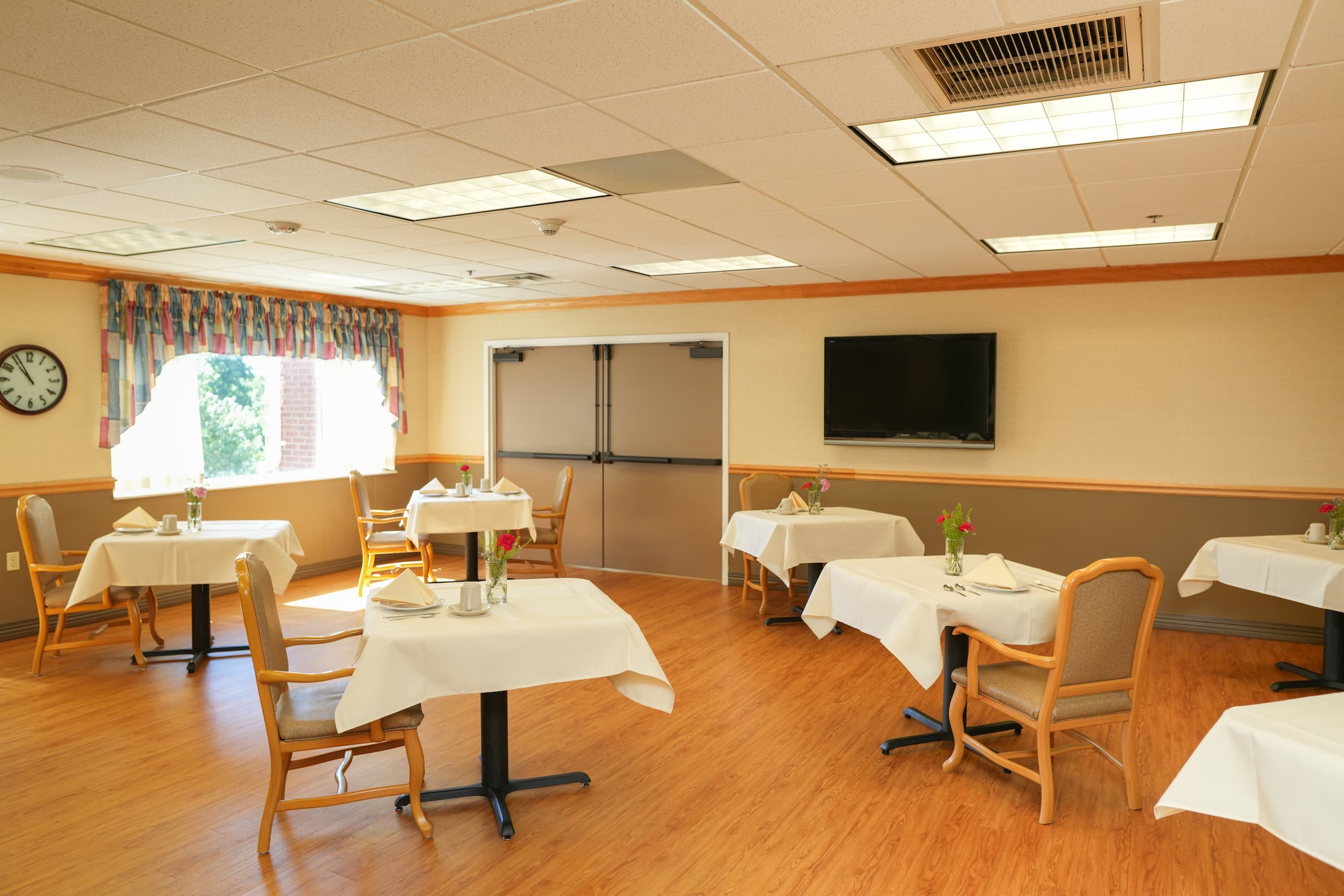 Dining area with tables set for meals, chairs, and a window with colorful curtains.