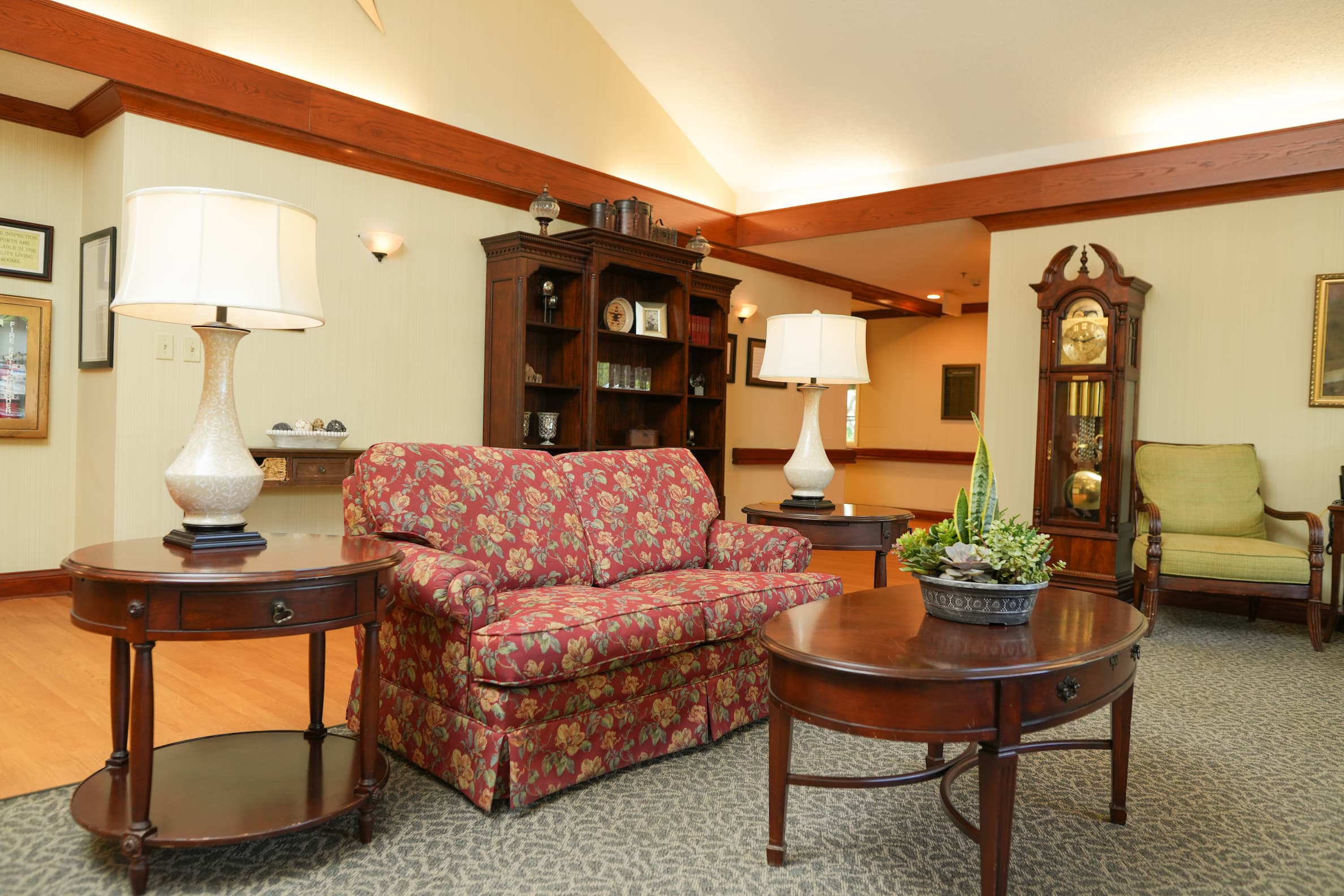 Cozy common area with floral sofa, wooden tables, and lamps in a living community.