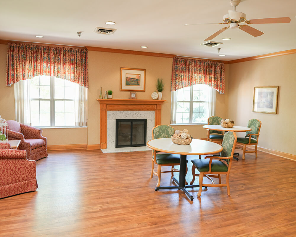 Spacious common area with armchairs, round tables, and a fireplace.