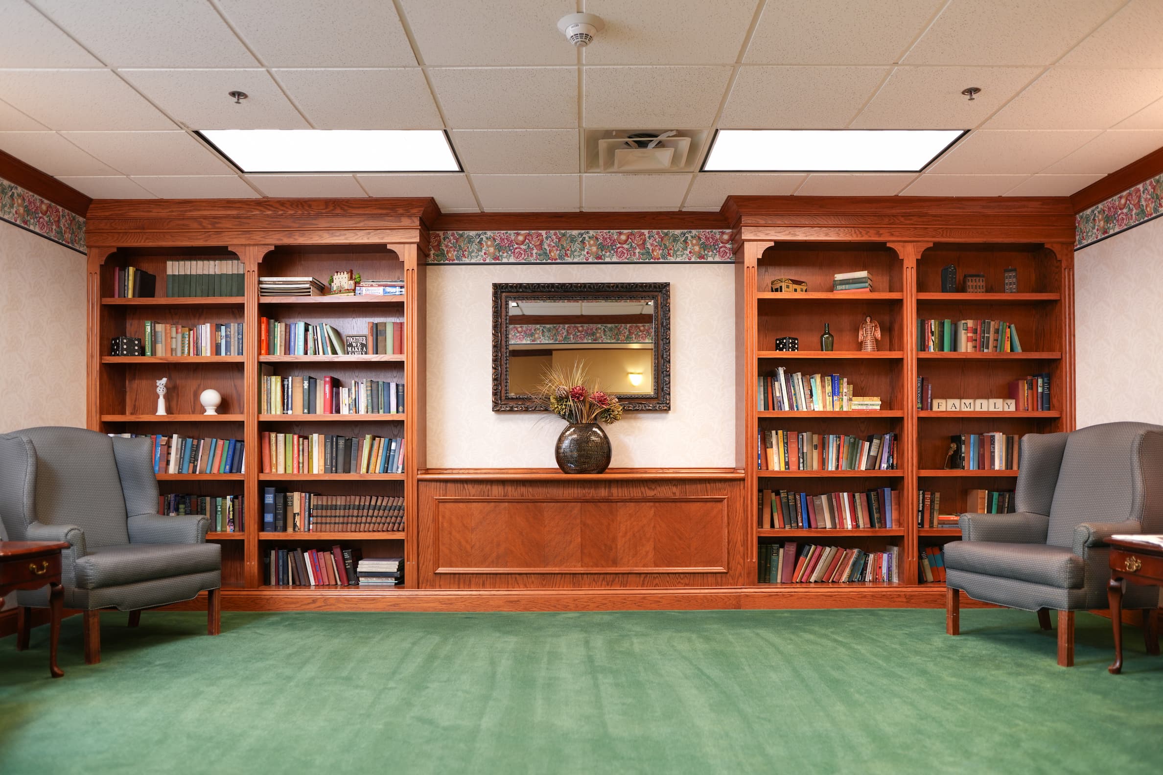 Cozy library area with bookshelves, armchairs, and a decorative mirror.