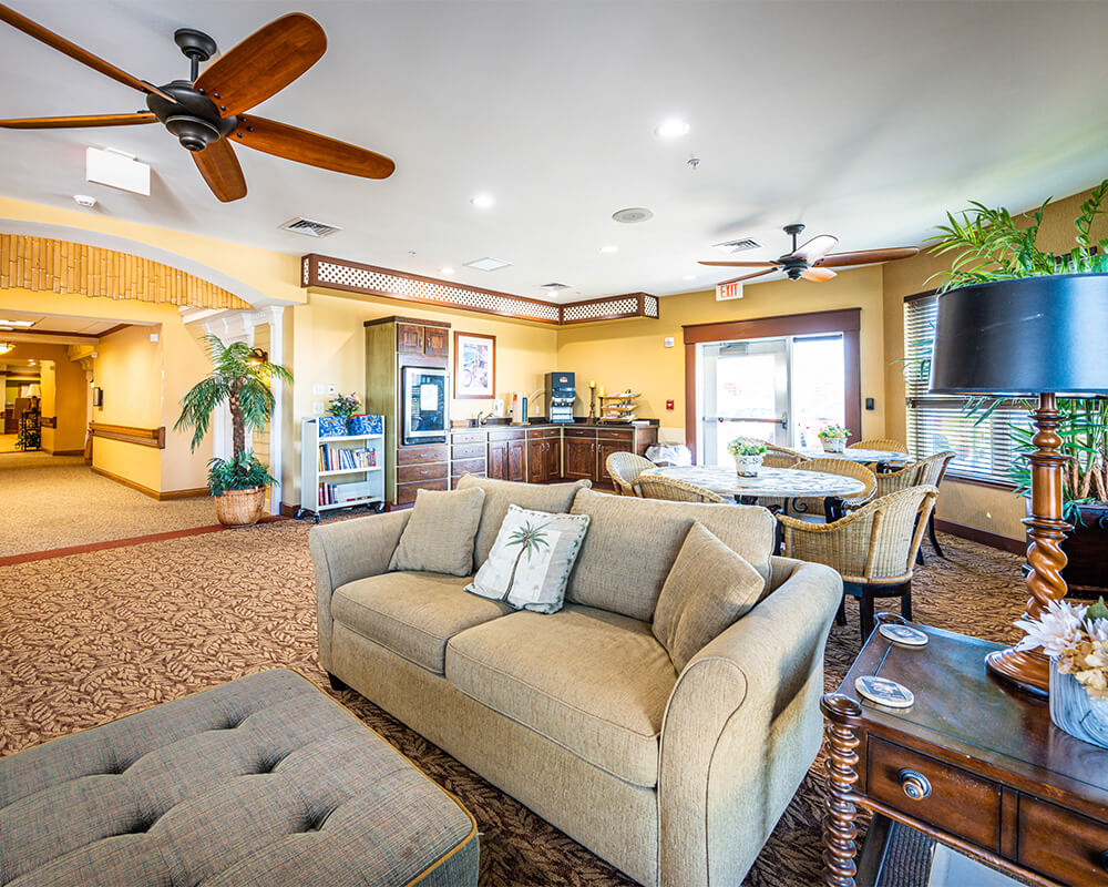 Spacious lounge with cozy seating and wicker dining set in a senior living unit.