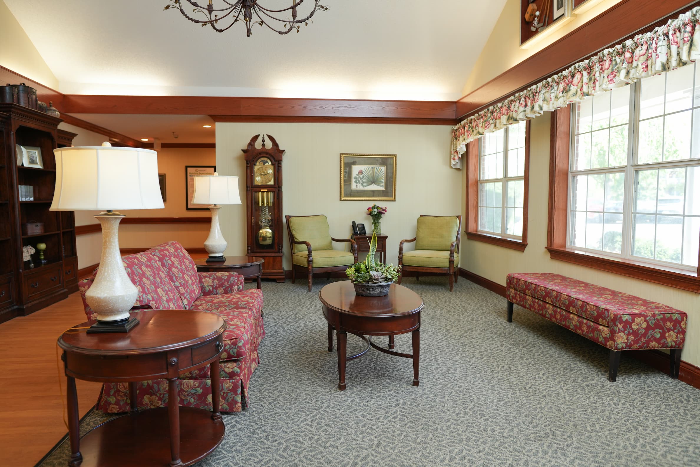 Cozy seating area with floral sofas and grandfather clock in community room.