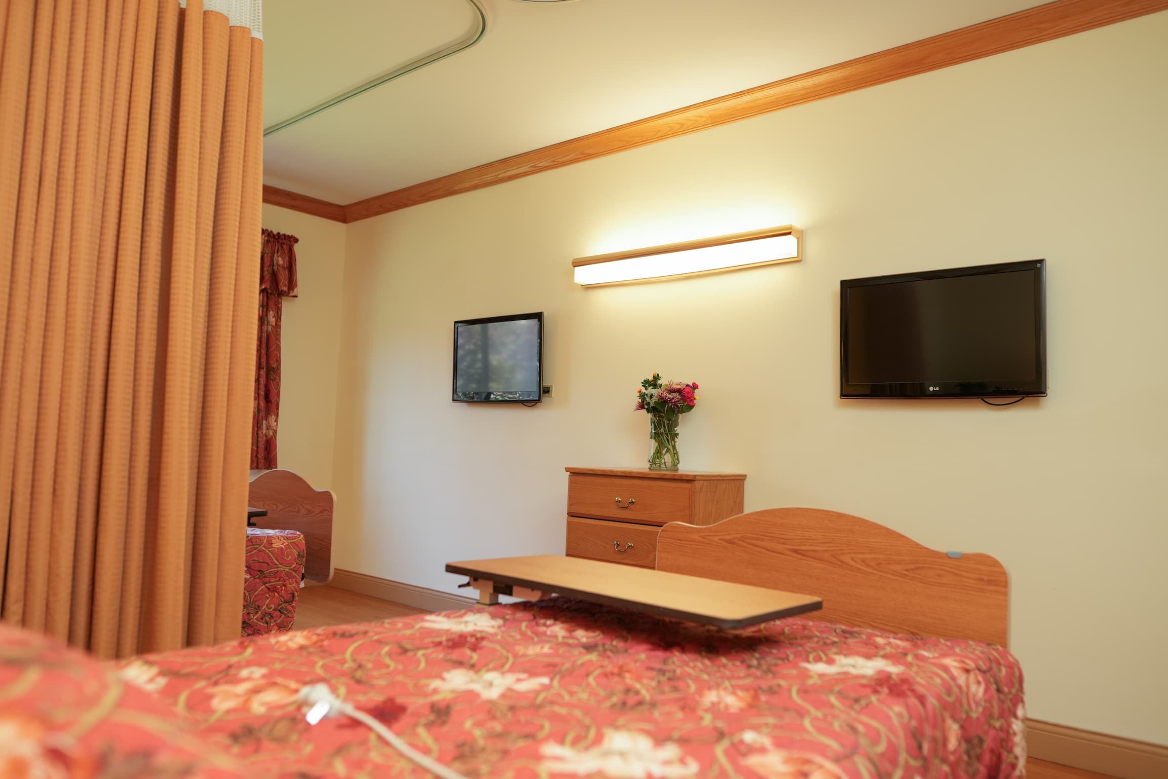 Comfortable senior living unit with twin beds, floral decor, and mounted TV.