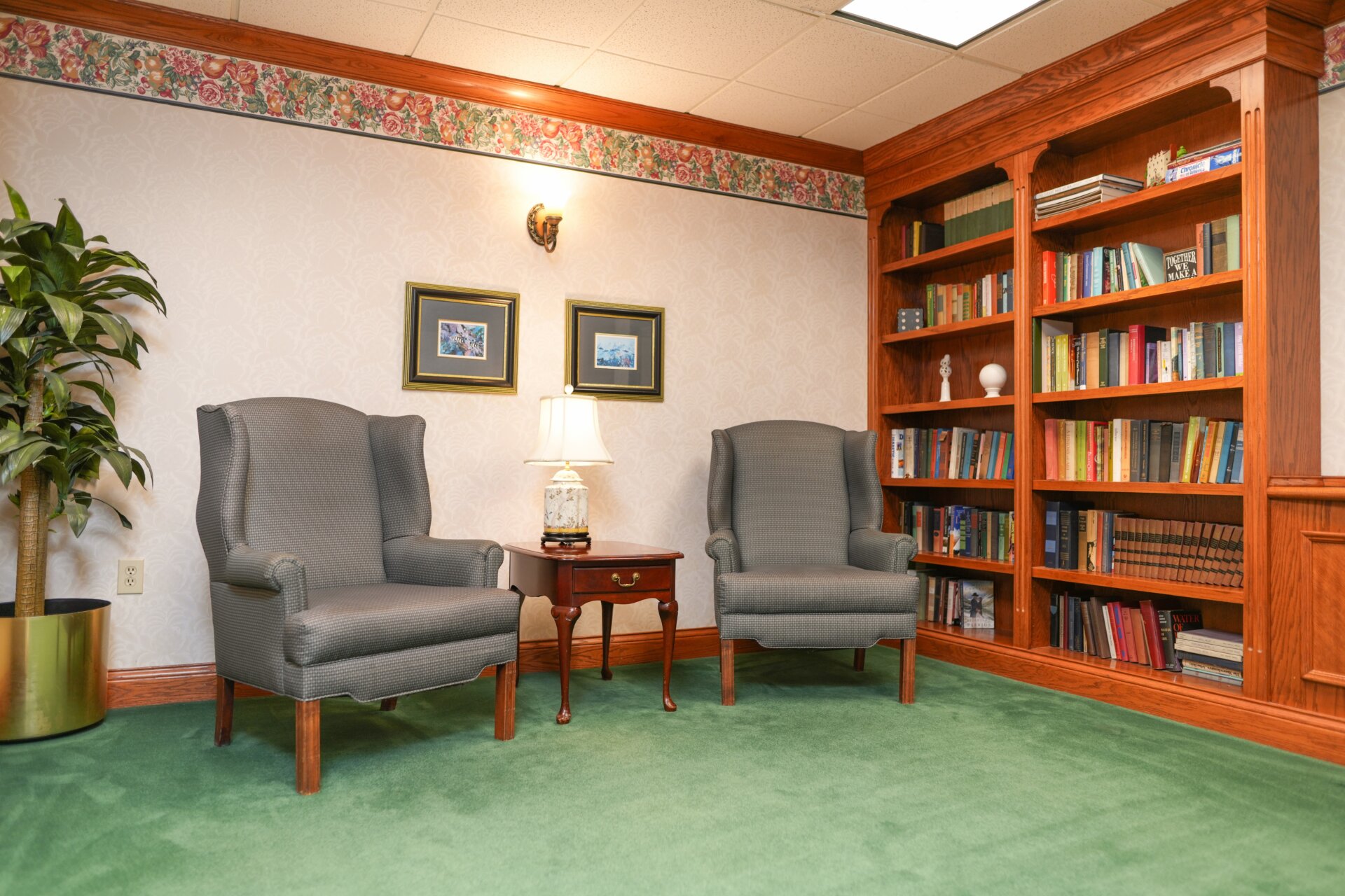 Cozy library corner with two chairs and wooden bookcase in a senior living unit.