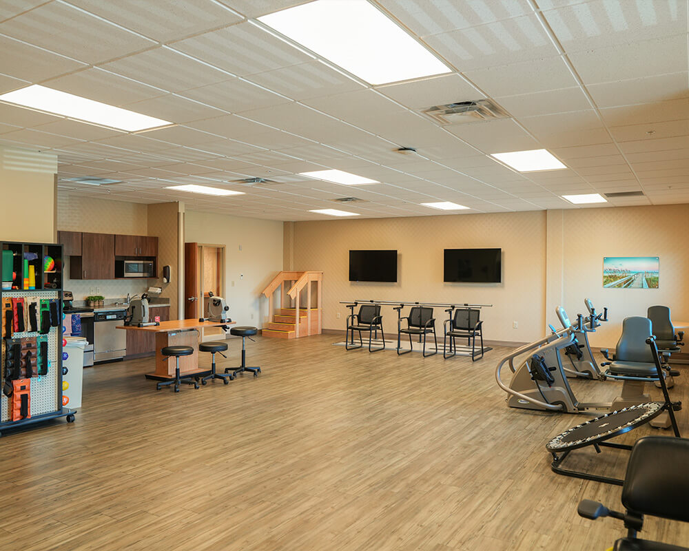Spacious gym with exercise equipment and kitchen in senior living building.