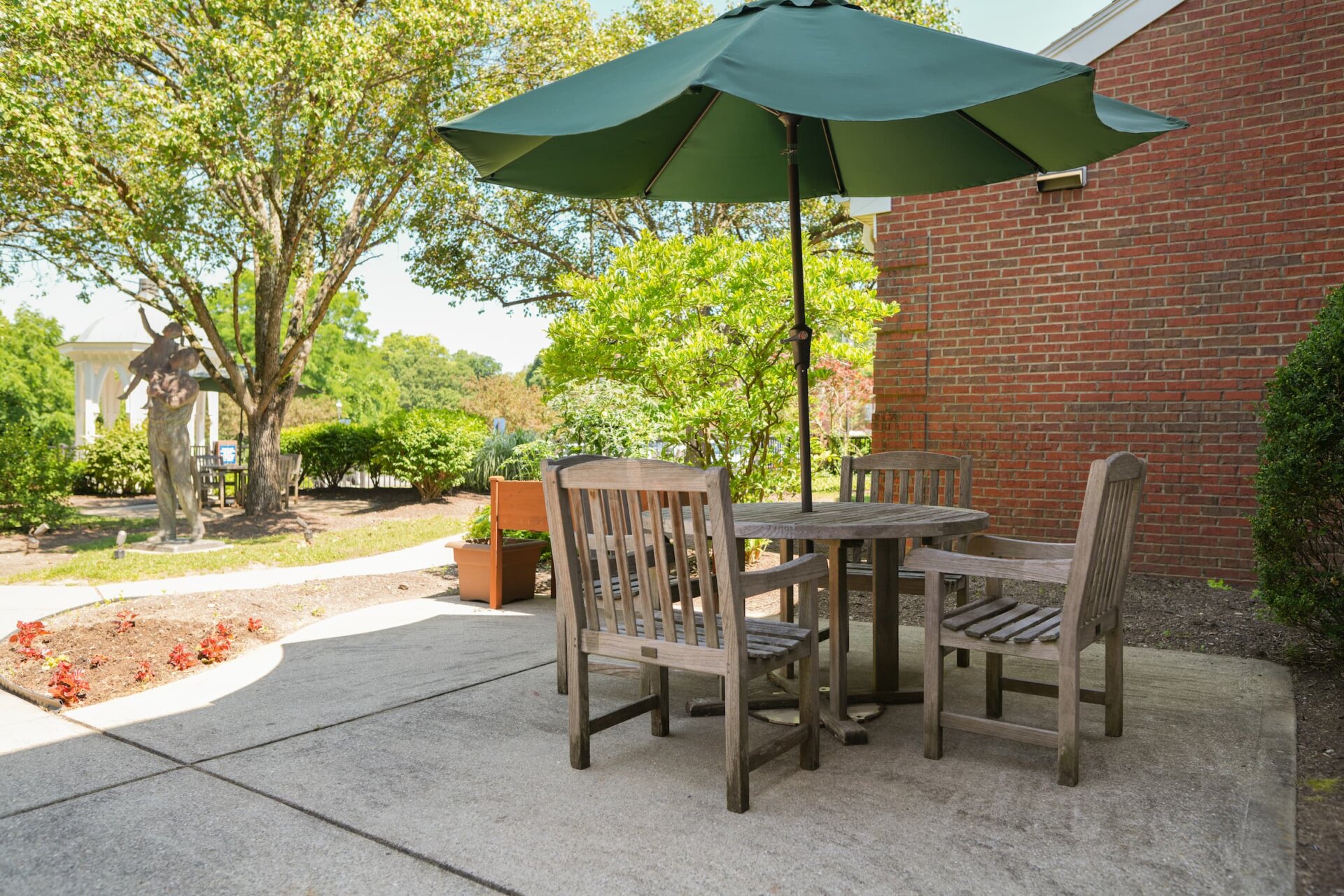 Outdoor patio with wooden seating and green umbrella, surrounded by lush greenery.