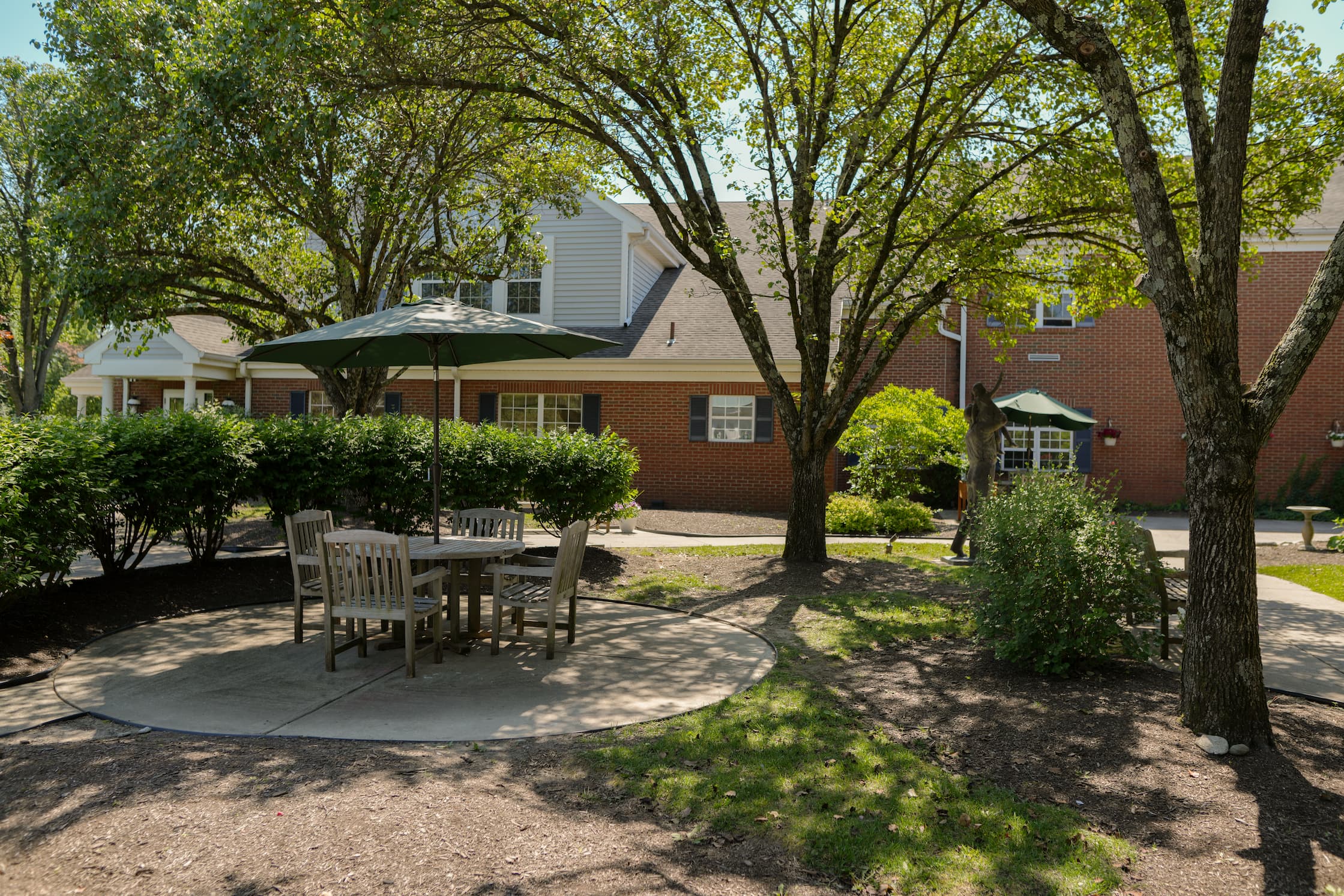Outdoor patio with tables under umbrellas, surrounded by trees and greenery.