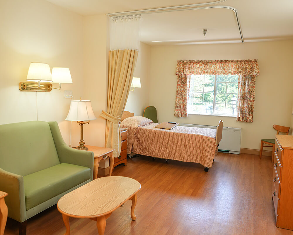 Comfortable unit with a bed, green chair, and window with floral curtains.