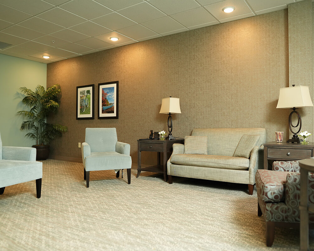 Comfortable seating area with sofas, chairs, and lamps in a senior living unit.