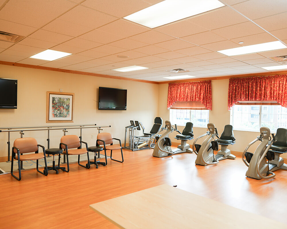 Therapy gym with exercise equipment and bright windows in senior living community.