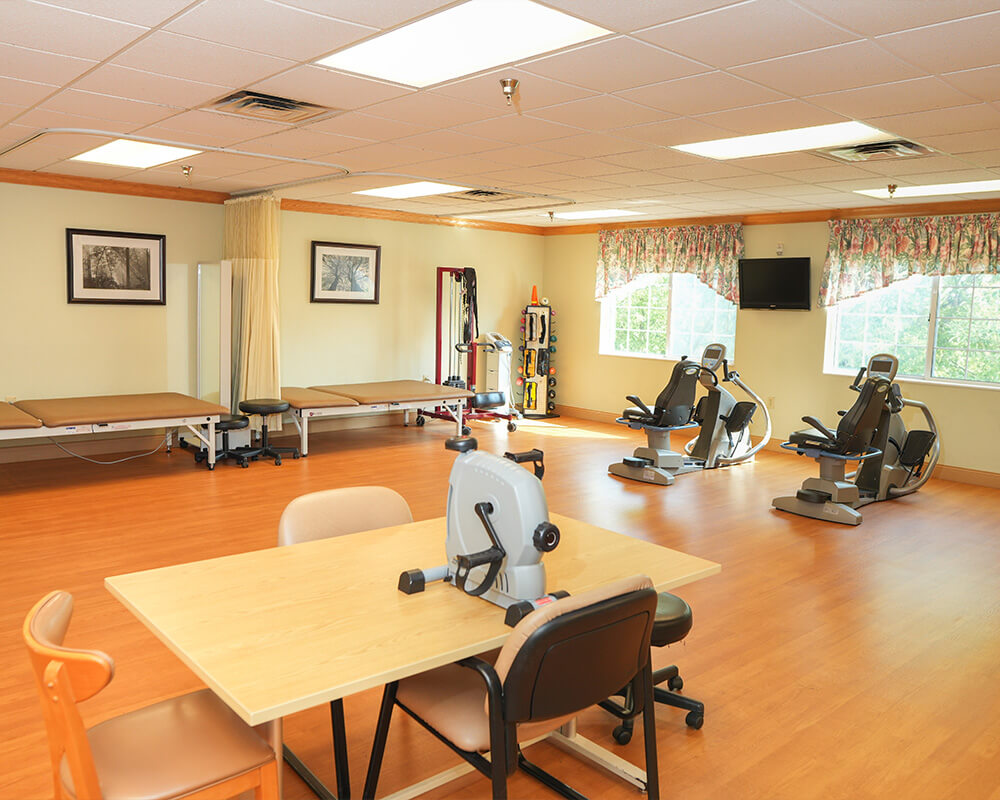 Therapy room with exercise equipment, therapy beds, and a table in a senior living unit.
