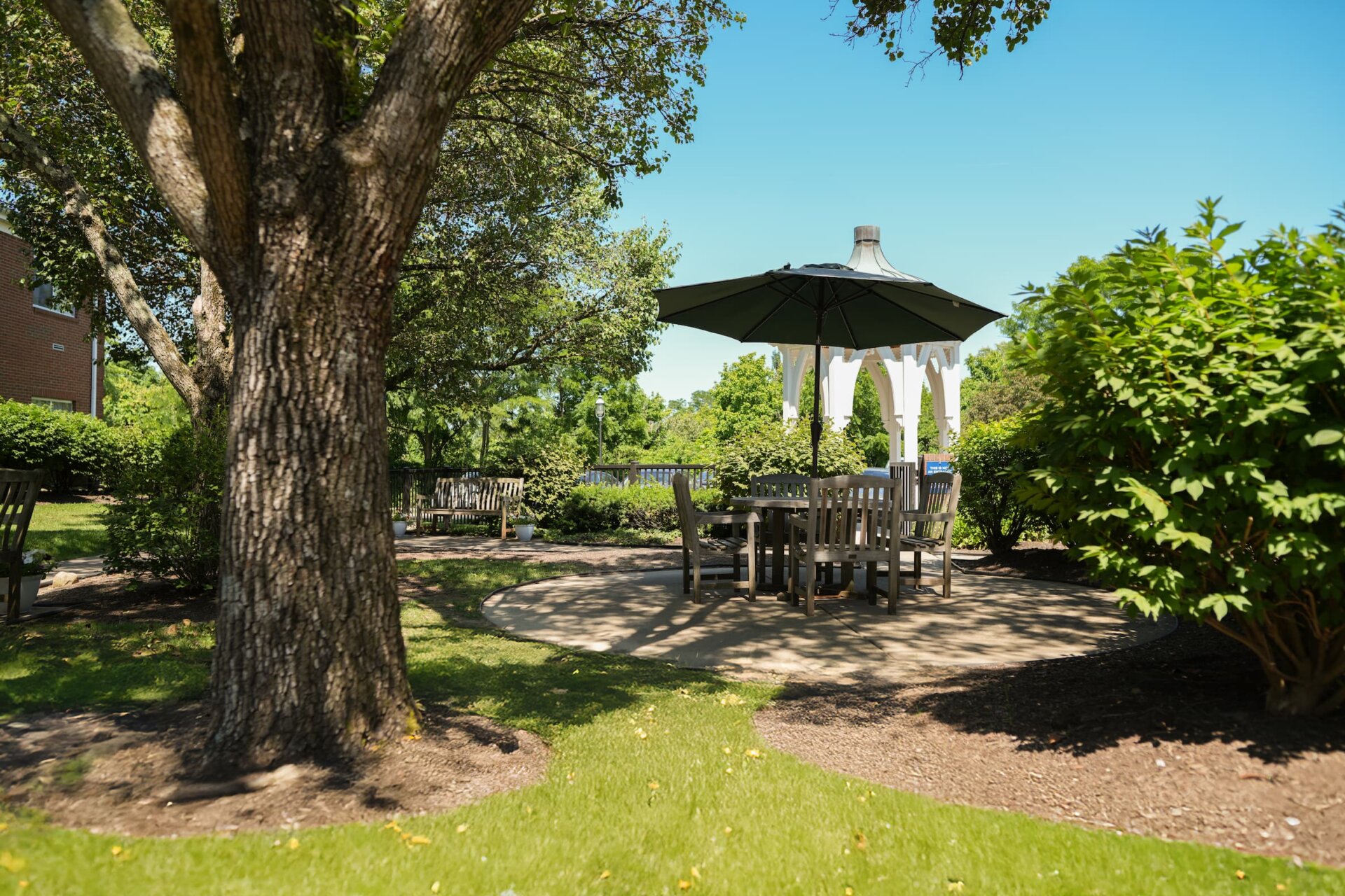 Shaded outdoor seating area with gazebo and tables in a tranquil garden.